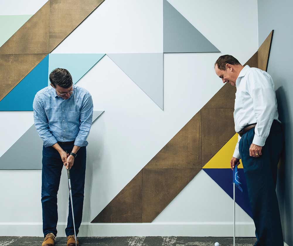 iMethods CEO putts a golf ball towards a hole on the in-house putt-putt course